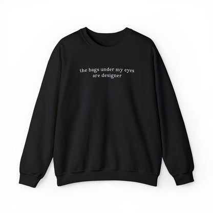A black oversized sweatshirt featuring minimalist white text across the chest that reads 'the bags under my eyes are designer'. Clean studio product photography on a white background for the Barely Sane clothing collection.