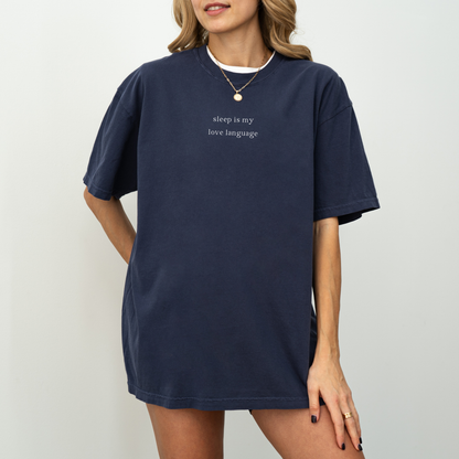A woman wearing a navy blue 'sleep is my love language' oversized t-shirt, accessorized with a gold necklace and a red string bracelet. Minimalist studio product photography for the Barely Sane clothing collection.