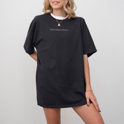 A woman wearing a black t-shirt with 'chief snack officer' text on a plain background