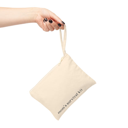 A woman's hand with black nail polish holding a cream canvas zipper pouch by its wristlet strap. The pouch features the text "mom's survival kit" printed on the front against a white background.
