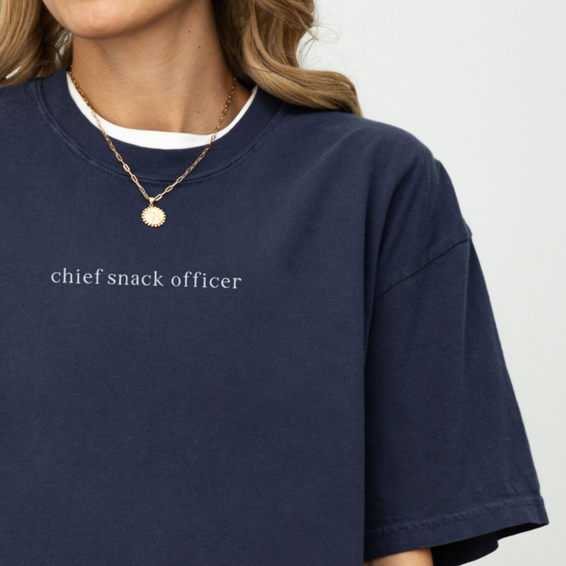 Navy blue t-shirt with 'chief snack officer' text worn by a woman on a studio set