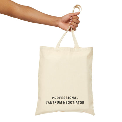 A hand holding the 'Professional Tantrum Negotiator' tote bag in natural cotton canvas. Minimalist typography design on a clean, isolated background for Barely Sane's parenting collection.